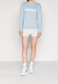 Light blue sweatshirt with white "adidas" logo, paired with white athletic shorts and white sneakers with black stripes.