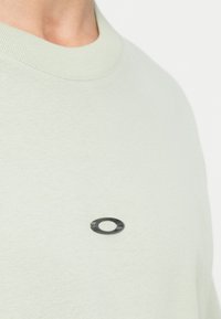 Ανοιχτό πράσινο φούτερ με ραμμένο ύφασμα και στρογγυλή λαιμόκοψη, διαθέτει μια μαύρη στρογγυλή ετικέτα στο στήθος. Μαλακό ύφασμα με λεία υφή.