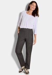 Witte blouse met driekwartmouwen, gecombineerd met donkere broek met houndstoothpatroon, afgewerkt met beige en zwarte sneakers.
