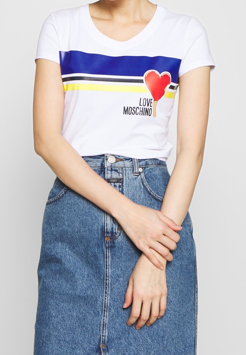 Bílý tričko s krátkým rukávem se modrými a žlutými vodorovnými pruhy, grafikou červeného srdce a textem "LOVE MOSCHINO". Nosit s džínovou sukní.