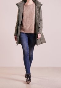 Sammetsgrön jacka med hög krage, beige stickad tröja och blå jeans. Svarta ankelboots fulländar outfiten.
