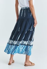 Falda maxi en azul oscuro con un diseño en capas; presenta patrones de teñido anudado en blanco y azul claro. Cintura elástica y tejido fluido.