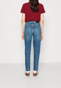 Camiseta de algodón roja oscura combinada con jeans de mezclilla azules de tiro alto, con corte recto y bolsillos minimalistas. Los zapatos son marrones y blancos.