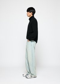 Svart strikket genser med høy krage, kombinert med lyseblå løstsittende jeans og hvite og svarte sneakers.