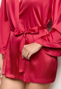 Ropa de satén en rojo brillante con mangas acampanadas fluidas, atada en la cintura con una cinta a juego, con una textura suave y de longitud corta.