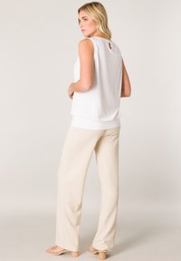 White sleeveless top with a back keyhole detail, paired with beige wide-leg pants and shoes featuring a chunky heel. Smooth fabric texture.
