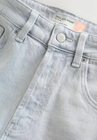 Short en jean bleu clair avec bouton en métal et étiquette indiquant "Timeless Short Mid Rise, Made in Bangladesh."