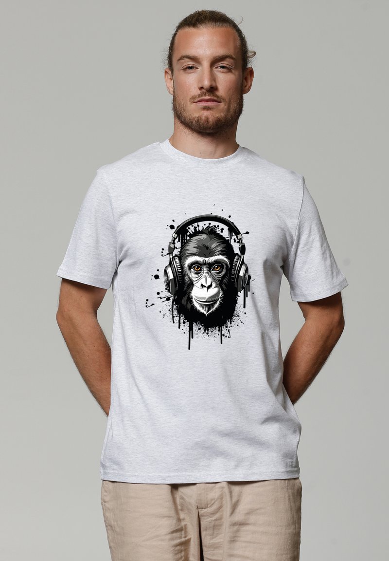 Homme aux cheveux attachés portant un t-shirt gris clair avec un visage de chimpanzé en noir et blanc, portant un casque audio et un motif d'éclaboussures de peinture.