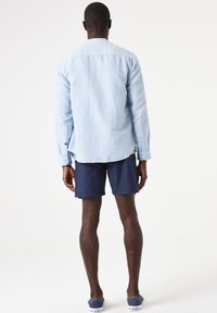 Lichtblauw overhemd met lange mouwen van een katoen-linnenmix, gecombineerd met marineblauwe shorts. Het overhemd heeft knoopmanchetten en een ontspannen pasvorm.