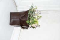 Brun, tekstureret lædertaske med en bred åbning, fyldt med forskellige grønne og pastelfarvede blomster, placeret mod en lysfarvet gulv.