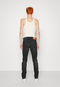 Svarta denimjeans med slim fit, med en brun läderpatch baktill, röd sömnad och en mjuk textur. Kombineras med en vit tanktop.