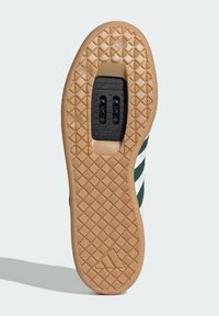 Schuhsohle mit einer strukturierten Gummirubber-Oberfläche. Verfügt über einen vertieften Bereich mit schwarzem Zubehör und zwei Löchern, umrandet von einem gemusterten Profildesign.