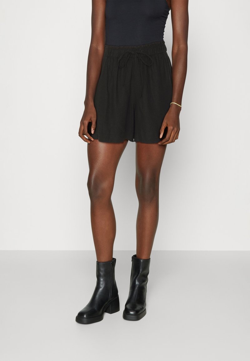 Shorts neri con cordino realizzati in tessuto leggero, con vita elastica. Abbinati a stivali neri alla caviglia con tacco spesso.