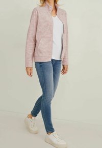 Lichtroze, ritsjack met een gestructureerde afwerking en zijzakken, gecombineerd met een witte T-shirt en blauwe skinny jeans. Witte sneakers maken de look af.
