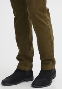 Olivově zelené slim-fit kalhoty v kombinaci s černými semišovými kotníkovými botami, se zdravým povrchem a jemnými švy, vhodné pro každodenní nošení.