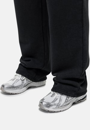 Scarpe sportive argento con dettagli in rete e una spessa suola bianca, indossate con pantaloni sportivi neri larghi, che coprono parzialmente la scarpa.