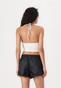 Svijetložuti halter crop top s vezanjem na leđima, uparen s crnim šortsevima s elastičnim pojasom. Glatka tkanina i jednostavan dizajn, bez vidljivih uzoraka.