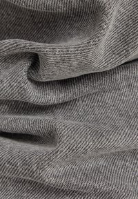 Tissu texturé gris avec un motif en chevrons, présentant des plis doux et un drapé naturel, mettant en valeur sa structure tissée et sa surface lisse.