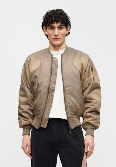 Μπουφάν bomber σε ανοιχτό καφέ χρώμα με αντιθετικά μπεζ μπαλώματα στους ώμους. Διαθέτει φερμουάρ στο μπροστινό μέρος, ριμπ μανσέτες και πλαϊνή τσέπη με φερμουάρ.