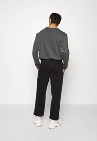 Węgiel-szary długi rękaw koszula z okrągłym dekoltem, w połączeniu z czarnymi spodniami zwężanymi i białymi trampkami. Gładkie kolory, casualowy krój, minimalistyczny design.