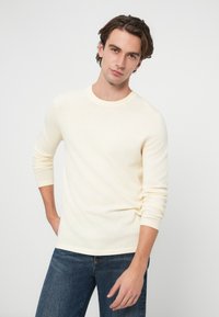 Jasnożółty sweter z długim rękawem i okrągłym dekoltem. Miękka tekstura i dopasowany krój, zestawiony z ciemnoniebieskimi jeansami. Minimalna ilość szwów i jednolity kolor.