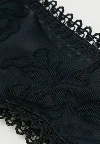 Svart spets tyg med ett intrikat blommönster, en texturerad yta och en delikat vågig kant.