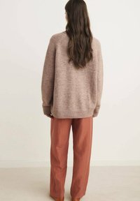 Maglione beige oversize a maglia con orlo a coste, abbinato a pantaloni larghi color ruggine, che mostrano una texture morbida e un fit rilassato.