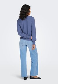 Maglione a coste blu in maglia con vestibilità morbida, abbinato a jeans a gamba larga color azzurro chiaro e ballerine nere, visto da dietro.