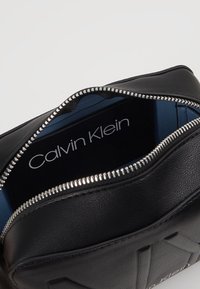 Borsa in pelle nera con superficie testurizzata e zip argentata. L'interno è dotato di una fodera azzurro chiaro e del logo "Calvin Klein".