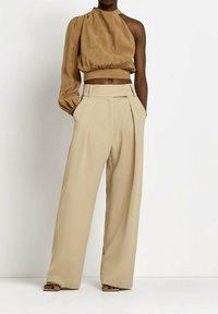 Brun, one-shoulder crop-top med en samlad textur, kombinerat med högmidjade, vida beige byxor med veck och fickor.