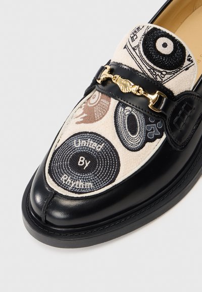 Svarta läderloafer med top i krämfärgad tyg som har broderade vinylskivor och texten "United By Rhythm", med detaljer i guldtonad metall i form av en hästbit.