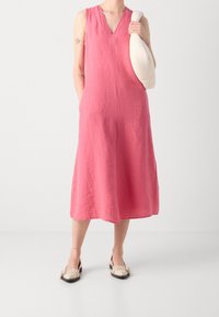 Pinkes Leinenkleid ohne Ärmel mit V-Ausschnitt und A-Linien-Silhouette. Kombiniert mit einer cremefarbenen Tasche und zweifarbigen Slippern, die subtile Texturen zur Geltung bringen.