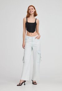 Top corto nero con spalline sottili, abbinato a pantaloni cargo larghi di un blu chiaro con tasche laterali e dettaglio con zip. Sandali neri con tacco.