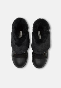 Bottes noires avec une tige duveteuse, en cuir et daim, avec des accents métalliques. Elles présentent un bout arrondi et une surface texturée.