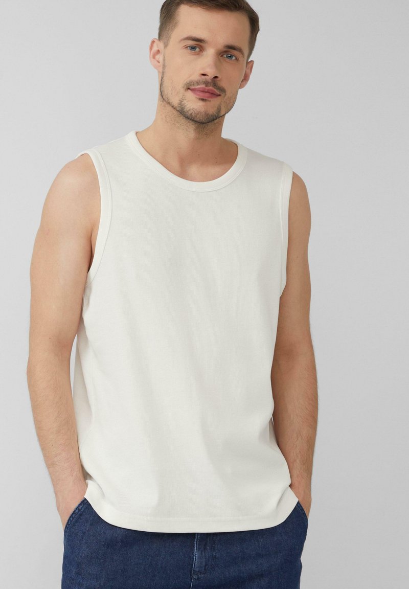 Weißes ärmelloses Tanktop aus geripptem Stoff, mit rundem Ausschnitt und lockerer Passform, kombiniert mit dunklen Jeans-Shorts.