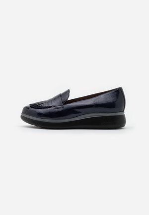 Mocassin bleu marine en cuir verni avec détail à franges et semelle épaisse noire, vue de côté sur fond blanc.