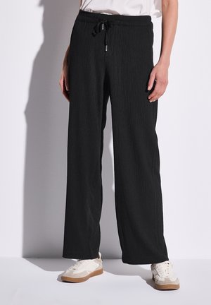 Pantalones de pierna ancha de canalé negros con cintura elástica y cordón, hechos de tejido texturizado. Combinados con zapatillas blancas.