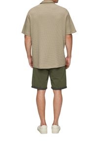 Beige gemustertes Kurzarmhemd mit einem lässigen Kragen, kombiniert mit olivgrünen Shorts und cremefarbenen Sneakern. Flacher Saum und umgeschlagene kurze Ärmel.