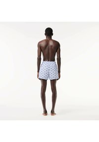 Costumi da bagno azzurri chiari con un motivo di piccole foglie verdi, cintura elastica e vestibilità comoda, mostrati da una vista posteriore.