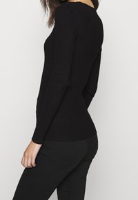 Haut noir à manches longues côtelé, ajusté à la taille, avec un col rond et une texture subtile. Associé à un jean noir pour compléter le look.