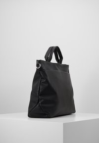 Černá kožená taška přes rameno s texturovaným povrchem, vybavená dvěma horními uchy a zapínáním na zip. Obsahuje boční kapsu.