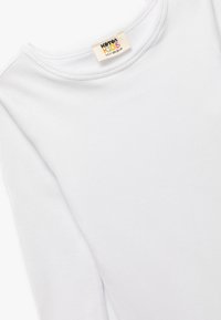Witte katoenen blouse met lange mouwen, een ribbelstructuur en een ronde hals. Etiket leest "KATTON KIDS S-V 90-110 CM."
