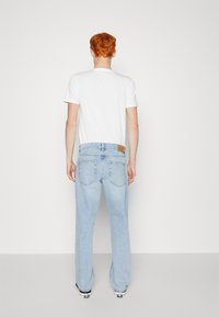 Light blue denim jeans with a relaxed fit, featuring a leather patch on the back waistband and two back pockets. White t-shirt is worn.