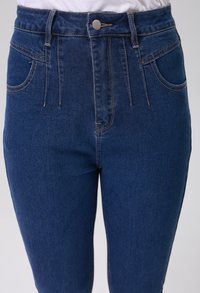Džínsy s vysokým pasem, modré, vyrobené z denimu, s pěti kapsami, měděným prošitím a kovovým knoflíkem na zapínání v pase.