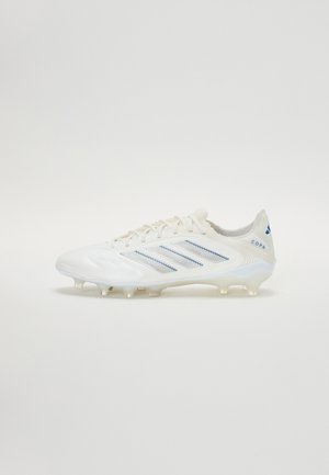 Weiße Fußballschuhe mit einer strukturierten Oberfläche, die blaue horizontale Streifen aufweist, einen gepolsterten Kragen und eine transparente Außensohle mit Stollen.
