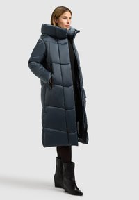 Dlhý námornícky modrý vatovaný kabát s vysokým golierom, diagonálnym prešívaním, prednými vreckami na zips a lesklým povrchom. Nosí sa cez čierne oblečenie a čižmy.