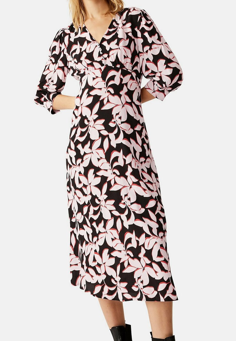 Robe noire avec un motif floral blanc et rose, décolleté en V, manches trois-quarts et longueur midi. Texture de tissu douce.