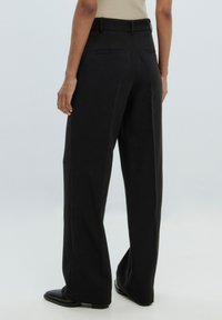Zwarte wijde broek gemaakt van gladde stof, met een middelhoge tailleband, twee achterzakken en een rechte snit, gecombineerd met zwarte schoenen.
