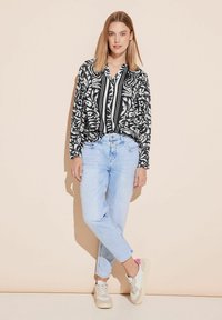 Blusa floreale in bianco e nero con scollo a V, abbinata a jeans dritti di colore azzurro chiaro e sneakers bianche con dettagli rosa.