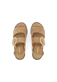 Sandales en suede marron avec un bout arrondi, deux sangles et une grande boucle circulaire. La semelle est texturée et légèrement surélevée.